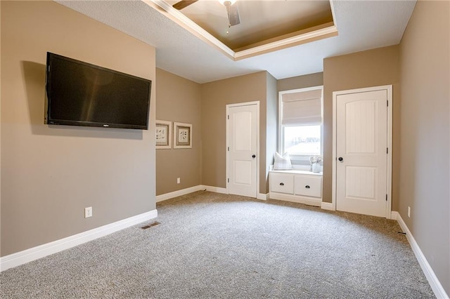 unfurnished bedroom with ceiling fan, a tray ceiling, and carpet