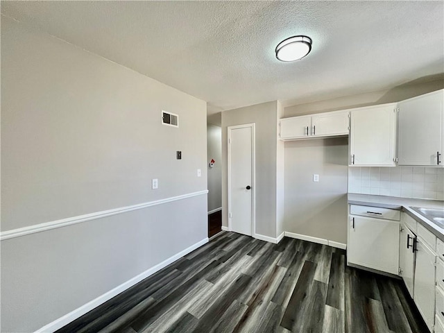 kitchen with backsplash, dark hardwood / wood-style flooring, white cabinets, and a textured ceiling