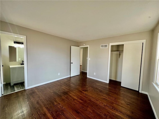 unfurnished bedroom featuring dark hardwood / wood-style floors, ensuite bath, and a closet