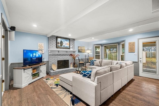 living room featuring a brick fireplace, wood-type flooring, and beamed ceiling