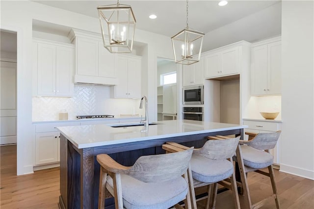 4218 W 158th Ter, Overland Park, KS 66224 - kitchen with stainless steel appliances, a kitchen island with sink, white cabinetry, light wood-style floors, and recessed lighting