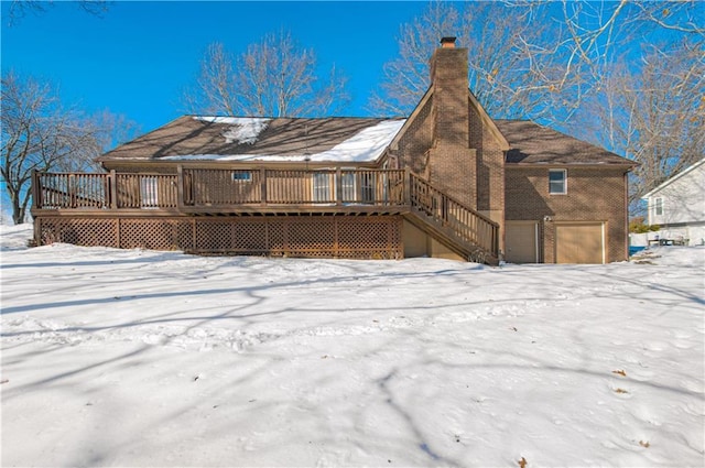 snow covered back of property with a garage and a deck