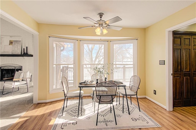 dining space with ceiling fan, light hardwood / wood-style flooring, and a fireplace