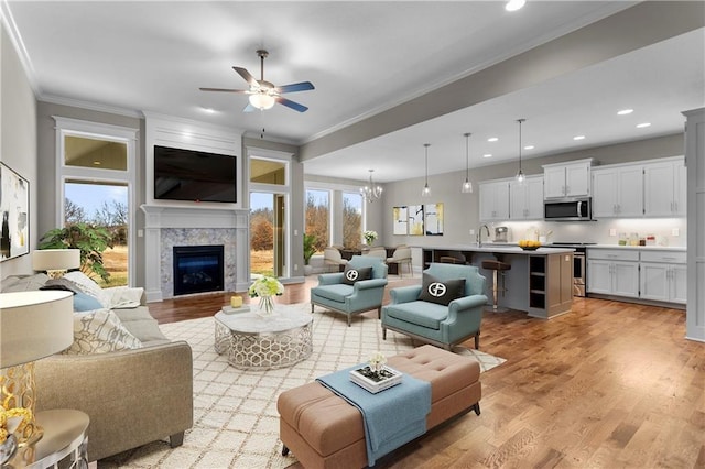 living room with ceiling fan with notable chandelier, light hardwood / wood-style floors, crown molding, and a fireplace