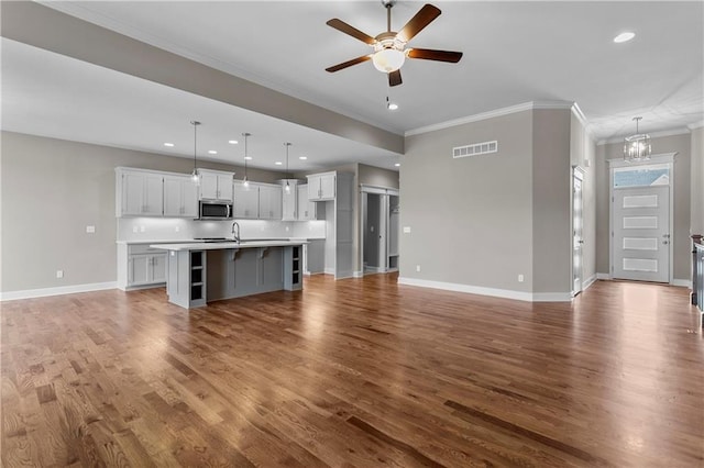 unfurnished living room with sink, wood-type flooring, ceiling fan with notable chandelier, and ornamental molding