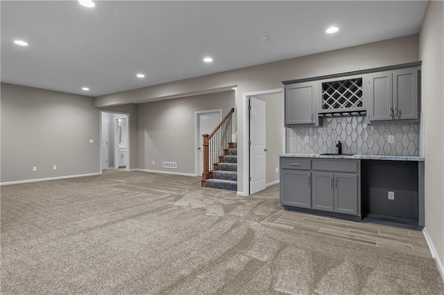 interior space featuring light carpet, tasteful backsplash, light stone counters, sink, and gray cabinets