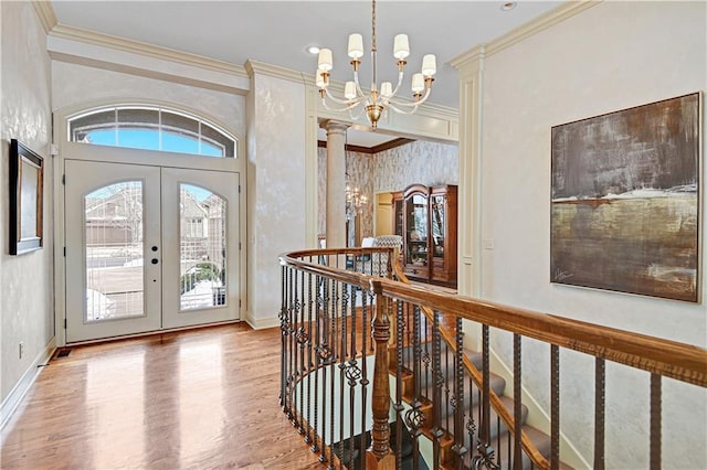 entryway with french doors, crown molding, a chandelier, and decorative columns