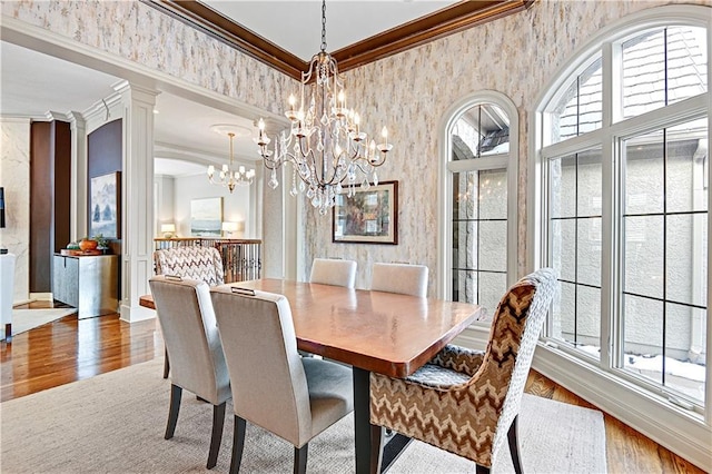 dining area featuring a notable chandelier, wood-type flooring, ornamental molding, and decorative columns