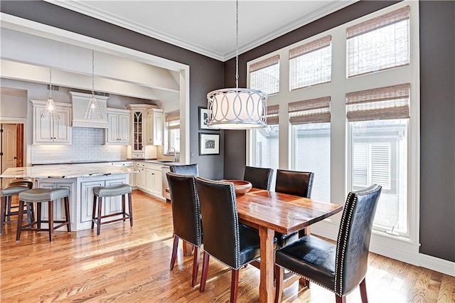 dining space featuring ornamental molding, sink, and light hardwood / wood-style flooring