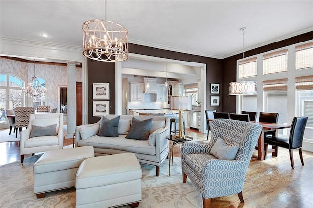 living room with crown molding, a chandelier, light hardwood / wood-style floors, and ornate columns