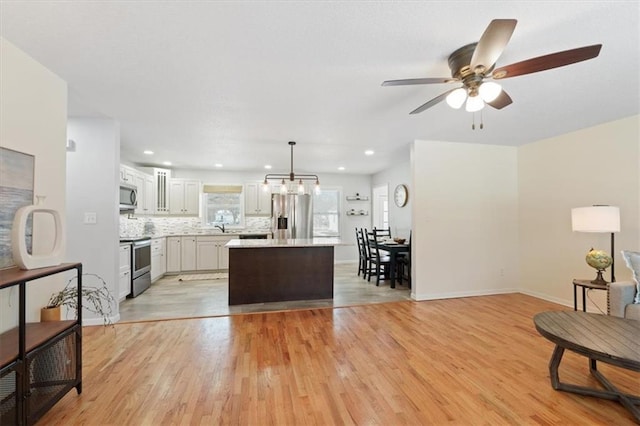 kitchen with a center island, hanging light fixtures, stainless steel appliances, light hardwood / wood-style floors, and decorative backsplash