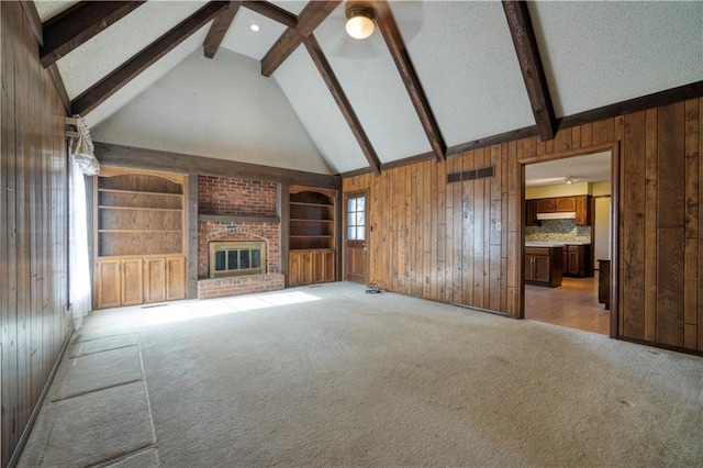 unfurnished living room with beam ceiling, wood walls, a fireplace, and light colored carpet