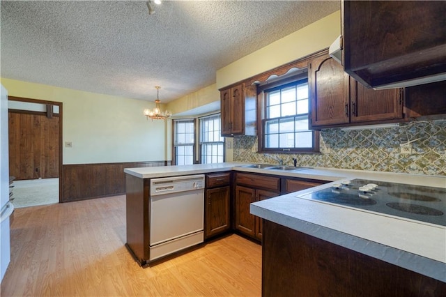 kitchen featuring a wainscoted wall, dishwasher, light wood-type flooring, a peninsula, and a sink