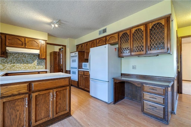 kitchen featuring under cabinet range hood, visible vents, white appliances, and light wood finished floors