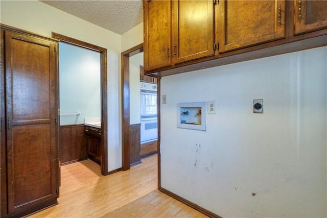 washroom featuring hookup for an electric dryer, cabinet space, washer hookup, a textured ceiling, and light wood-type flooring