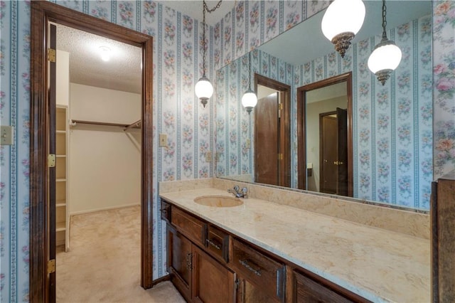 bathroom with a spacious closet, a textured ceiling, and wallpapered walls