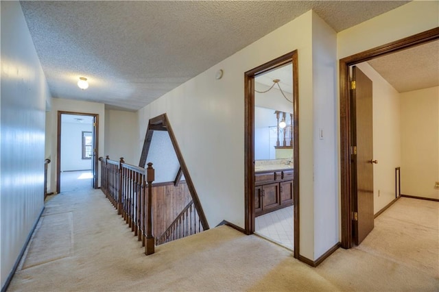 corridor featuring light carpet, an upstairs landing, a textured ceiling, and baseboards