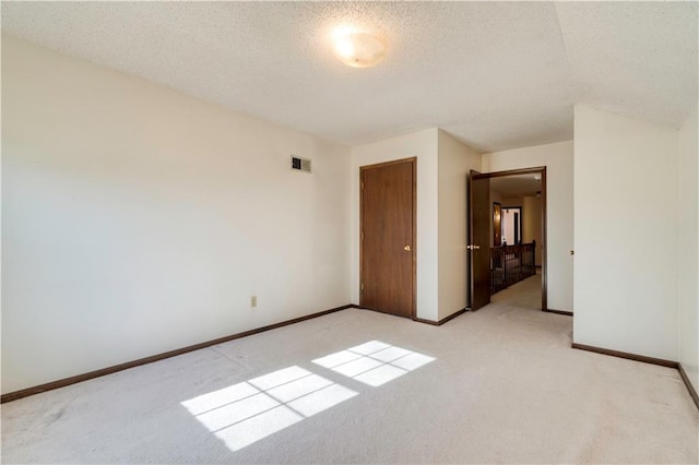 unfurnished room with light carpet, visible vents, a textured ceiling, and baseboards