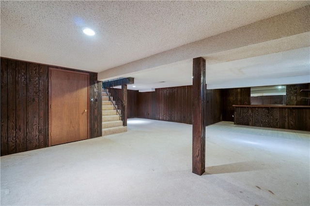 finished basement featuring wooden walls, stairs, carpet flooring, a textured ceiling, and a bar