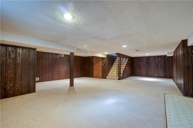 finished below grade area with a textured ceiling, wood walls, stairs, and carpet