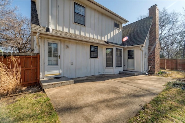 view of front of house featuring fence, board and batten siding, roof with shingles, and a chimney