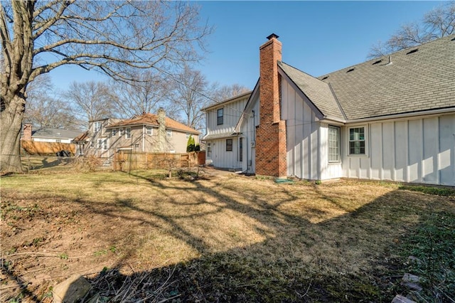 rear view of house with a shingled roof, a yard, board and batten siding, and a chimney