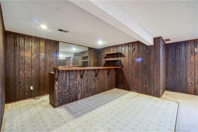 bar with a bar, visible vents, wood walls, and a textured ceiling