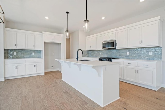 kitchen featuring white cabinets, pendant lighting, an island with sink, and sink