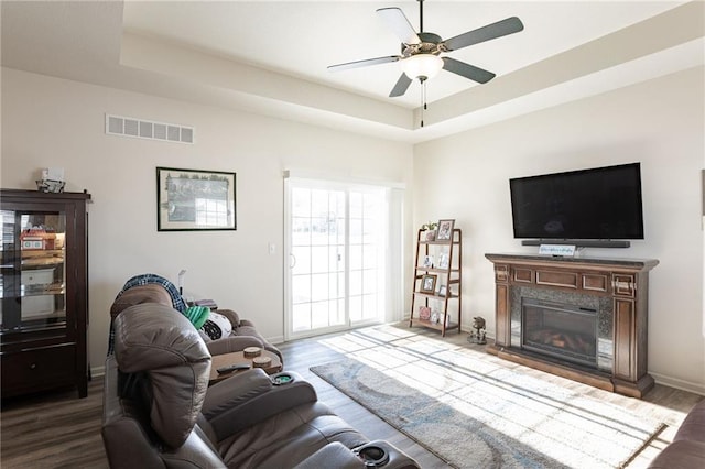 living room featuring a tray ceiling, a premium fireplace, ceiling fan, and wood-type flooring