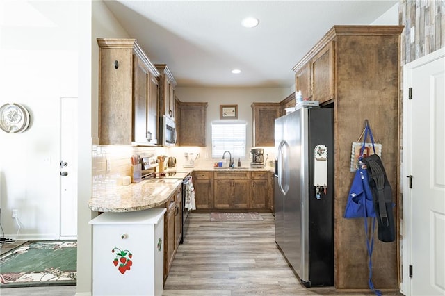 kitchen with light stone countertops, decorative backsplash, stainless steel appliances, sink, and light hardwood / wood-style flooring