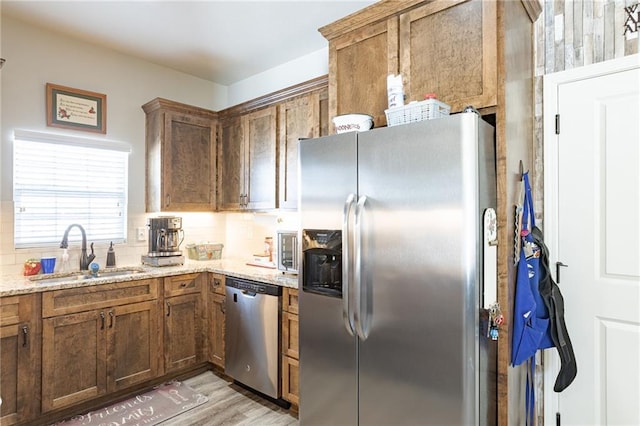 kitchen with sink, light hardwood / wood-style flooring, appliances with stainless steel finishes, tasteful backsplash, and light stone counters