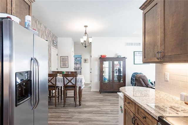 kitchen featuring light stone countertops, an inviting chandelier, stainless steel refrigerator with ice dispenser, backsplash, and light wood-type flooring