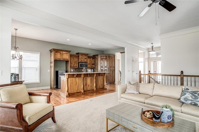 living room with ceiling fan with notable chandelier, light hardwood / wood-style floors, and crown molding