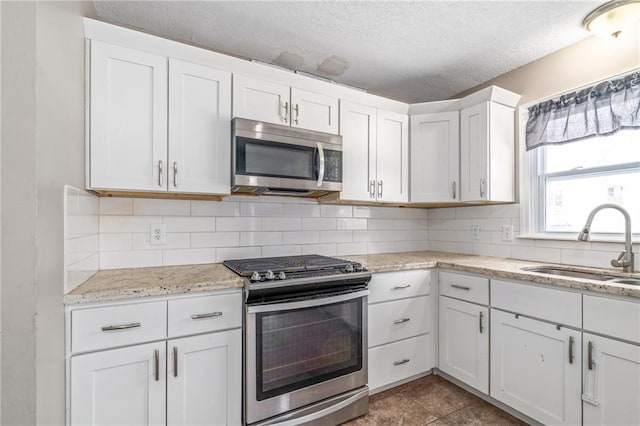 kitchen with sink, stainless steel appliances, a textured ceiling, decorative backsplash, and white cabinets