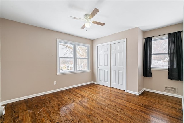 unfurnished bedroom with multiple windows, dark hardwood / wood-style flooring, a closet, and ceiling fan