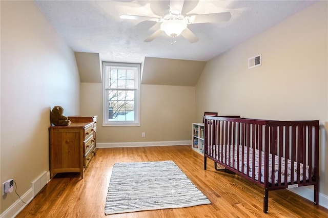 bedroom with a crib, ceiling fan, lofted ceiling, and hardwood / wood-style flooring