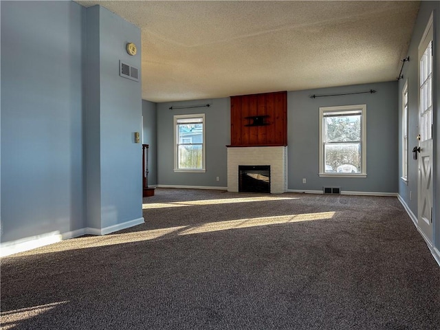 unfurnished living room with a fireplace, a textured ceiling, carpet floors, and plenty of natural light