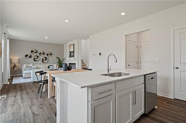 kitchen featuring open floor plan, light countertops, stainless steel dishwasher, wood finished floors, and a sink