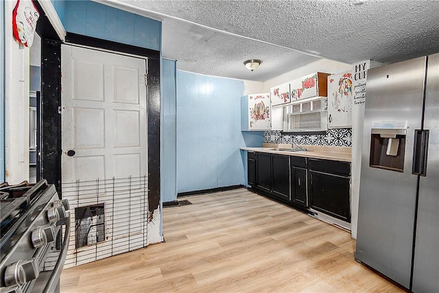 kitchen featuring sink, stainless steel refrigerator with ice dispenser, light hardwood / wood-style floors, a textured ceiling, and decorative backsplash