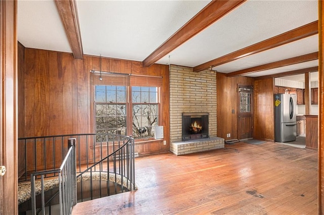 unfurnished living room featuring wood walls, a fireplace, beamed ceiling, and light hardwood / wood-style flooring