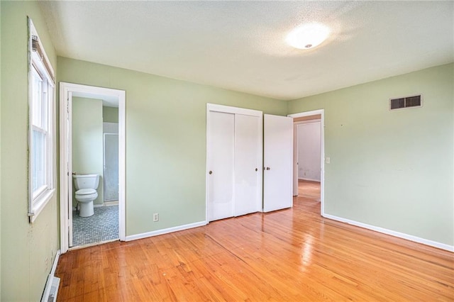 unfurnished bedroom with ensuite bathroom, light hardwood / wood-style floors, and a closet