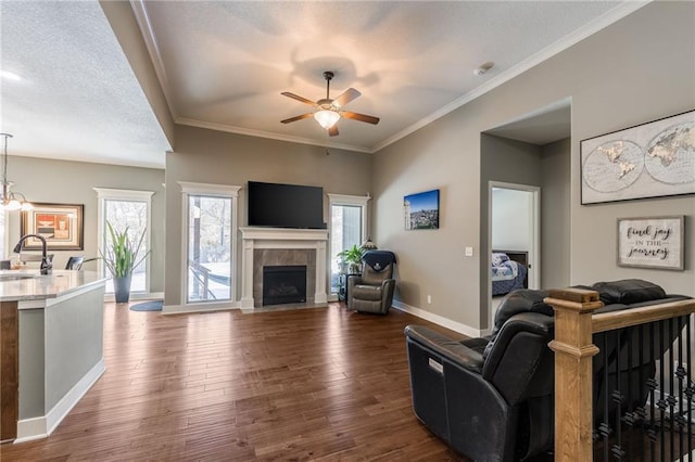 living room featuring sink, dark wood-type flooring, a textured ceiling, a tiled fireplace, and ceiling fan with notable chandelier