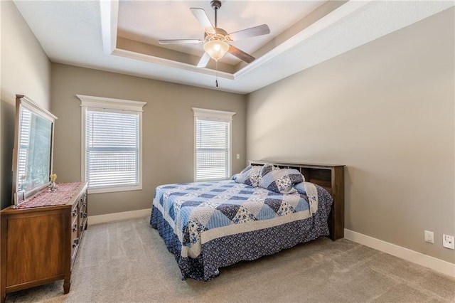 carpeted bedroom with a raised ceiling and ceiling fan