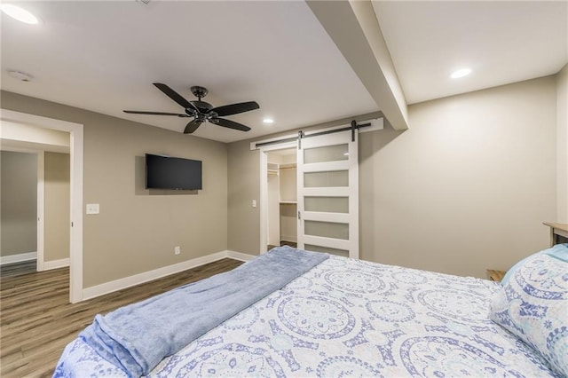 bedroom with hardwood / wood-style flooring, ceiling fan, a barn door, a spacious closet, and a closet