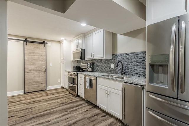 kitchen with sink, a barn door, appliances with stainless steel finishes, light stone counters, and white cabinetry