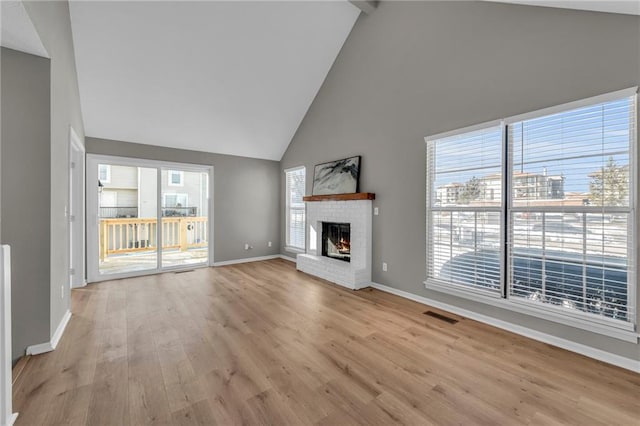 unfurnished living room with a fireplace, beam ceiling, light wood-type flooring, and high vaulted ceiling