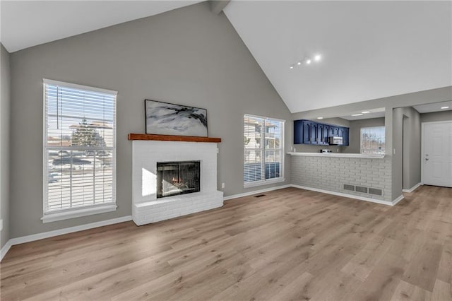 unfurnished living room featuring light wood-type flooring, high vaulted ceiling, a brick fireplace, and a healthy amount of sunlight