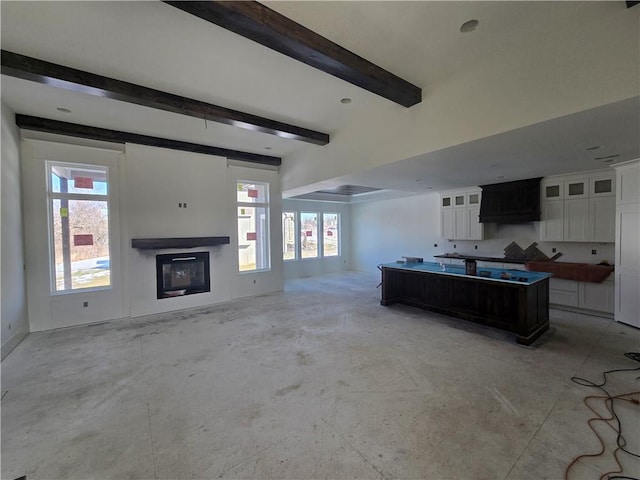 kitchen with white cabinets, dark brown cabinets, an island with sink, and beamed ceiling