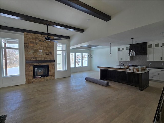 living room featuring a stone fireplace, a ceiling fan, beam ceiling, and a healthy amount of sunlight