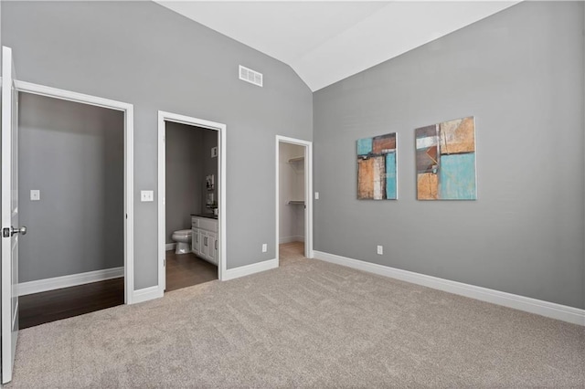 unfurnished bedroom featuring lofted ceiling, ensuite bath, carpet, a walk in closet, and a closet